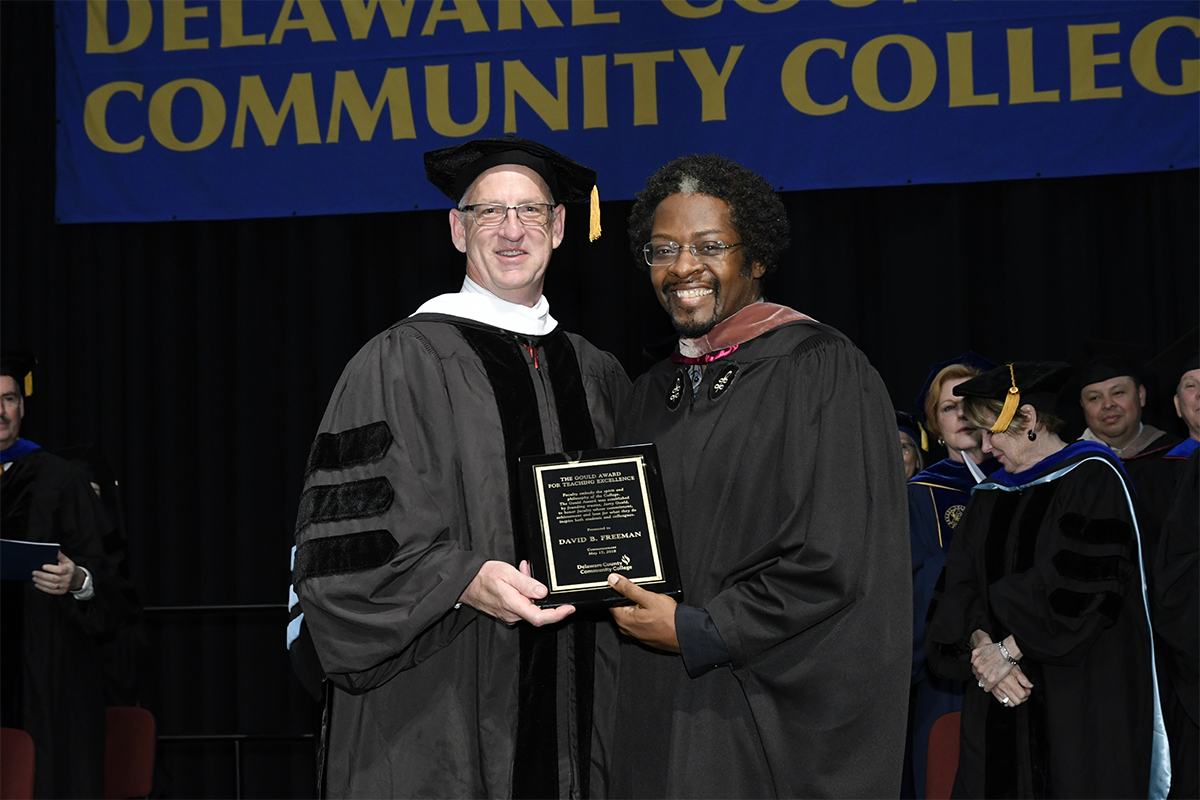 Associate Professor of English Dr. David Freeman (right) receives the 2018 Gould Award for Excellence in Teaching from Michael Ranck, chairman of the Board of Trustees of Delaware County Community College, at the College’s 2018 Commencement ceremony which was held at West Chester University.
